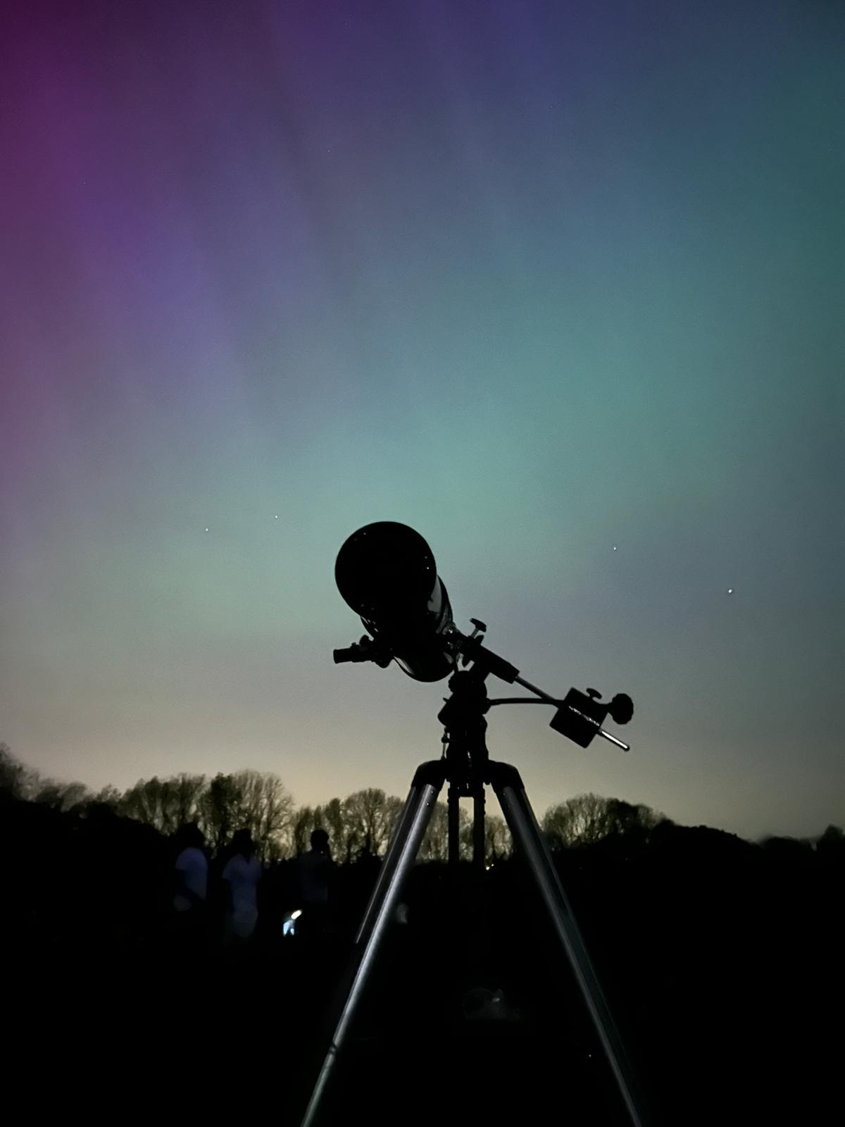 The SpaceSoc telescope, shrouded in darkness, contrasts the bright aurora in the background.